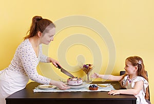A young mother and her little daughter cutting a cake for a birthday party