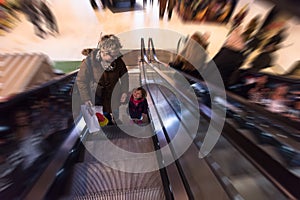 Young mother and her little daughter on escalator in shopping mall