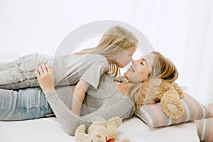 Young mother and her little daughter hugging and kissing on bed