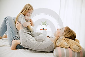 Young mother and her little daughter hugging and kissing on bed