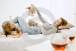 Young mother and her little daughter hugging and kissing on bed