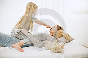 Young mother and her little daughter hugging and kissing on bed