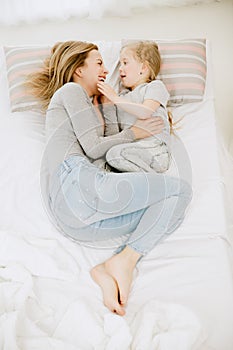 Young mother and her little daughter hugging and kissing on bed