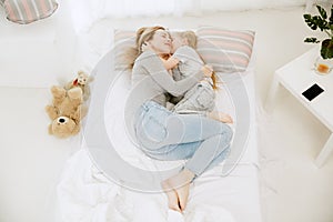 Young mother and her little daughter hugging and kissing on bed