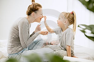 Young mother and her little daughter hugging and kissing on bed