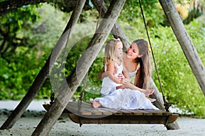 Young mother and her little daughter swinging