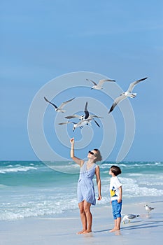 Young mother and her little son feeding seagulls on tropical beach, Florida photo