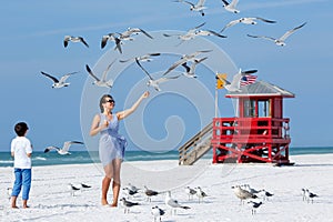 Young mother and her little son feeding seagulls on tropical beach photo