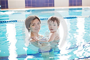 Young mother and her son having fun in a swimming pool. Healthy family mother teaching baby swimming pool