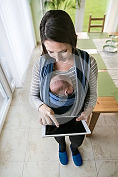 Young mother with her son in sling, holding tablet