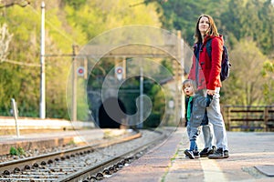 Young mother and her toddler son on a railway station. Mom and little child waiting for a train on a platform. Family ready to