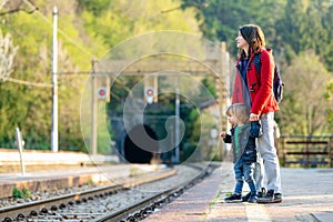 Young mother and her toddler son on a railway station. Mom and little child waiting for a train on a platform. Family ready to