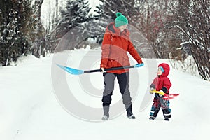 Young mother and her toddler son stand with snow shovels on rural road. Winter seasonal concept