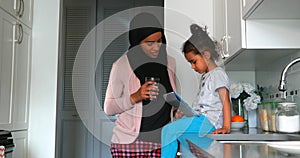 Young mother with a hijab drinking a glass of water near her daughter in the kitchen 4k