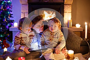 Young mother and his two little children sitting by a fireplace at home on Christmas time