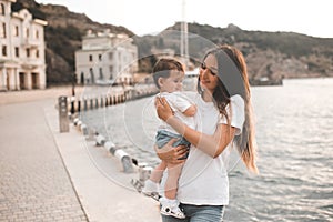 Young mother hold baby girl 1 year old wear casual clothes walk in city street over seafront.