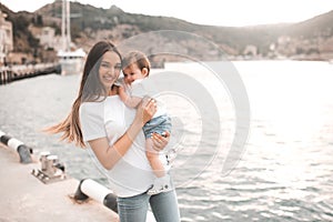 Young mother hold baby girl 1 year old wear casual clothes walk in city street over seafront.