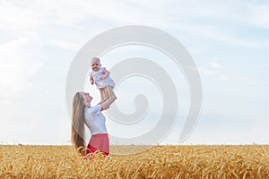 Young mother holding baby in her arms in wheat field. Vacation with children in countryside