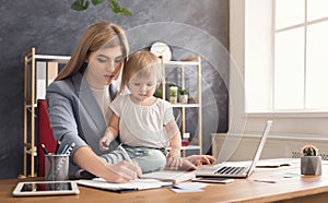 Young mother holding baby while writing notes