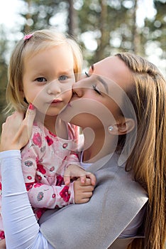 Young mother holding cute toddler girl daughter in her arms and giving her a kiss on a cheek