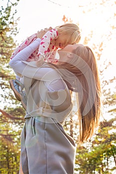 Young mother holding cute toddler girl daughter in her arms and lifting her up in the air, both laughing