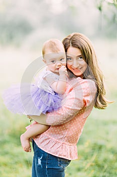 Young mother holding daughter in her arms. Beautiful Mother And Baby outdoors. Nature. Beauty Mum and her Child playing