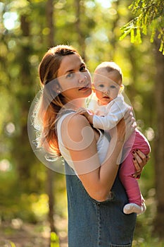 Young mother holding daughter in her arms. mom kisses and plays with daughter in the summer. Happy family in the park