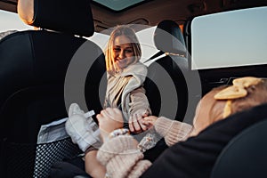 Young Mother Holding Her Baby Daughter by Hand While She Sitting in Child Car Seat in Car, Young Family on the Road Trip