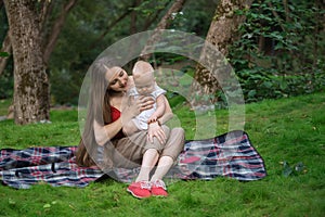 Young mother holding her baby in her arms and sitting on a picnic blanket. Happy motherhood