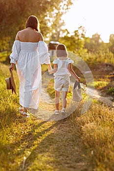 young mother is holding her child& x27;s daughter hand and walking in green meadow on a summer sunny day. Family