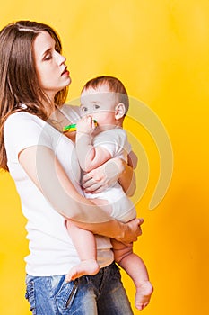 Young mother holding her child, on yellow background