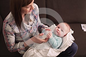 Young mother holding her infant baby son on her hands, feeding him milk from bottle