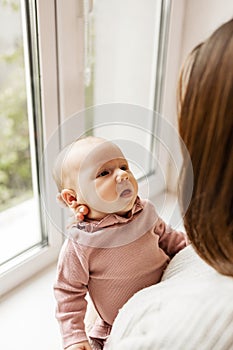 Young mother holding her newborn baby girl in her arms near window.