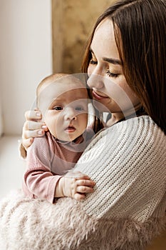 Young mother holding her newborn baby girl in her arms near window.