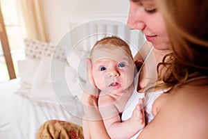 Young mother holding her newborn baby son, home bedroom