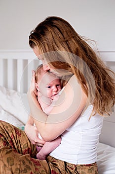 Young mother holding her newborn baby son, home bedroom