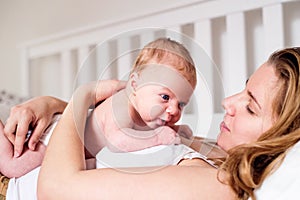 Young mother holding her newborn baby son, home bedroom