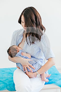 Young mother holding her newborn child. Mom nursing baby. Nursery interior. Young woman breastfeeding her baby girl