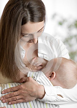 Young mother holding her newborn child. Mom nursing baby. Pretty woman breastfeeding kid.