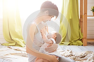 Young mother holding her newborn child. Mom nursing baby in a white bedroom. Nursery interior. Family at home