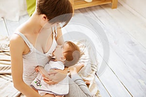 Young mother holding her newborn child. Mom nursing baby in a white bedroom. Nursery interior. Family at home
