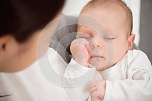 Young mother holding her newborn child. Mom nursing baby. Woman and new born boy relax in a white bedroom.