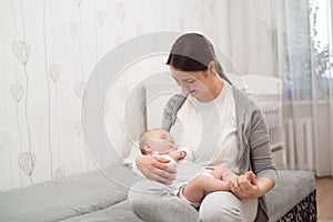 Young mother holding her newborn child. Mom nursing baby. Woman and new born boy relax in a white bedroom.