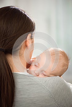 Young mother holding her newborn child. Mom nursing baby. Woman and new born boy relax in a white bedroom.