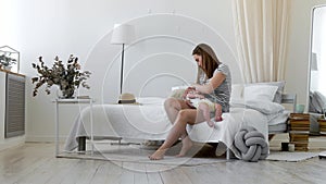 Young mother holding her newborn child. Mom nursing baby. Woman and new born boy relax in a white bedroom. Mother breast