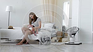 Young mother holding her newborn child. Mom nursing baby. Woman and new born boy relax in a white bedroom. Mother breast