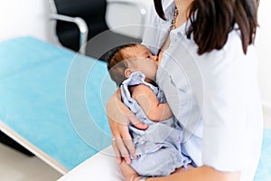 Young mother holding her newborn child. Mom nursing baby. Woman and new born boy relax in a white bedroom. Mother breast feeding