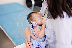 Young mother holding her newborn child. Mom nursing baby. Woman and new born boy relax in a white bedroom. Mother breast feeding