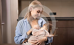 Young mother holding her newborn child. Mom nursing baby. Woman and new born boy relax in a white bedroom with rocking