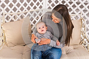 Young mother holding her newborn child. Mom nursing baby. Woman and new born boy in the room. Mother playing with